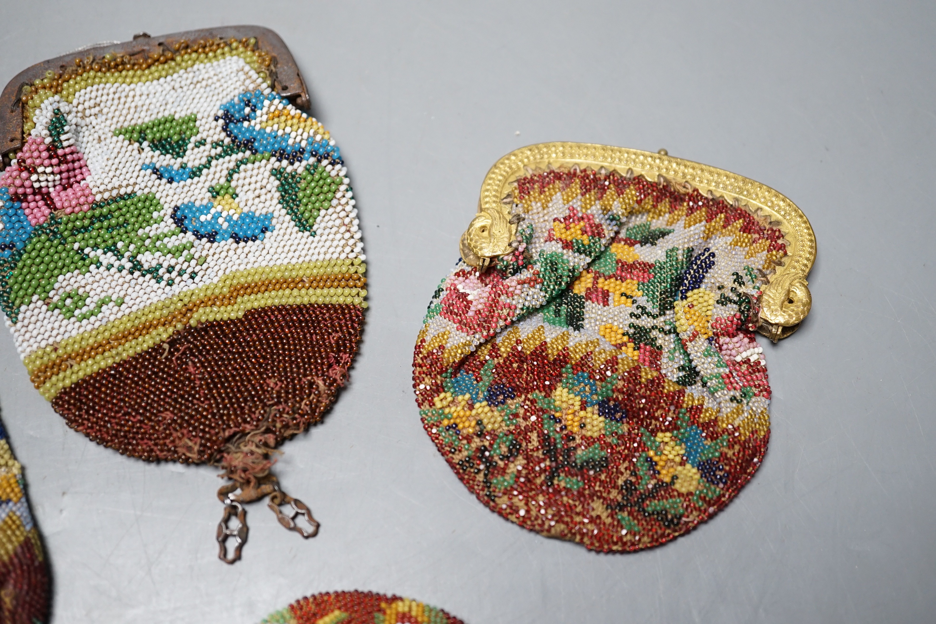 An early 19th century ornate gilt framed beaded bag with multi coloured floral design, together with three similar worked purses, gilt framed bag 20 cms high